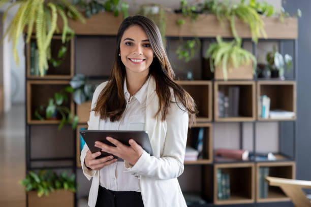 Portrait of a successful Latin American business woman using a tablet computer at the office and looking at the camera smiling